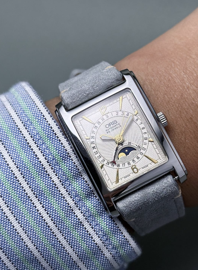 Oris rectangular moonphase automatic on a grey suede strap, worn under a striped shirt cuff