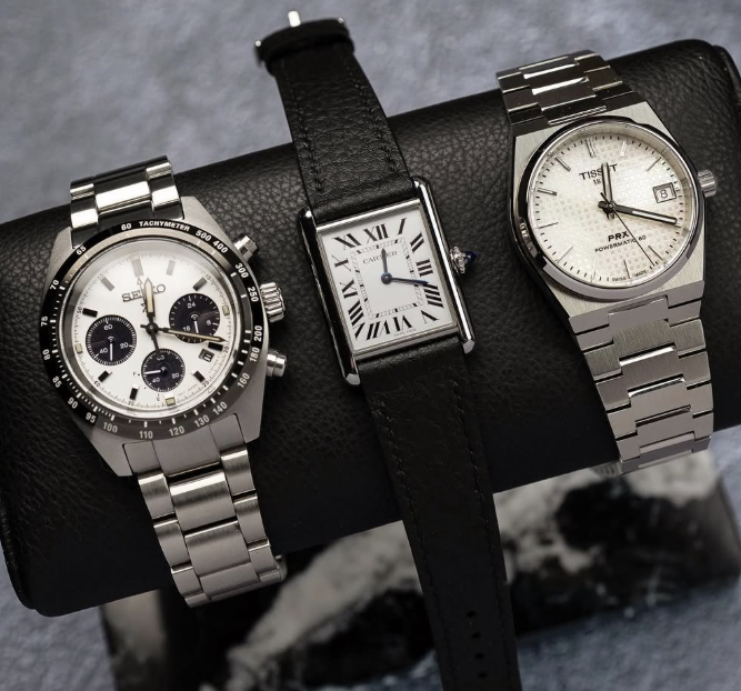 Three watches on a black leather roll -- Seiko panda chronograph, Cartier Tank, Tissot PRX Powermatic 80